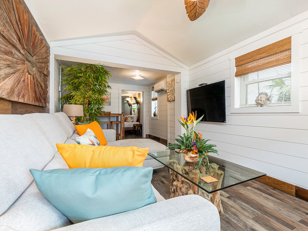 A modern living room with a grey sofa, a glass coffee table, and a large plant.