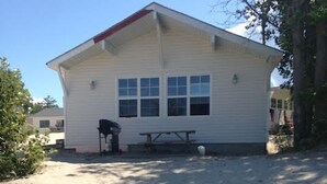 A single-story building with a flat roof and a small porch area. There is a picnic table and a grill on the porch. - BEACHFRONT COTTAGE IN WASAGA BEACH - SANDPIPER BEACH RESORT - COTTAGE # 2 (Wasaga Beach)
