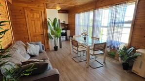 A cozy cabin interior with a wooden ceiling, a dining area with a table and chairs, a sofa with cushions, and a kitchen in the background. - BEACHFRONT COTTAGE IN WASAGA BEACH - SANDPIPER BEACH RESORT - COTTAGE # 2 (Wasaga Beach)