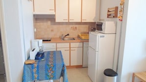 A compact kitchen with white cabinets, a microwave, a sink, and a small table with a blue tablecloth. - Cozy apartment near thermal baths, pets allowed (Balaruc-les-Bains)