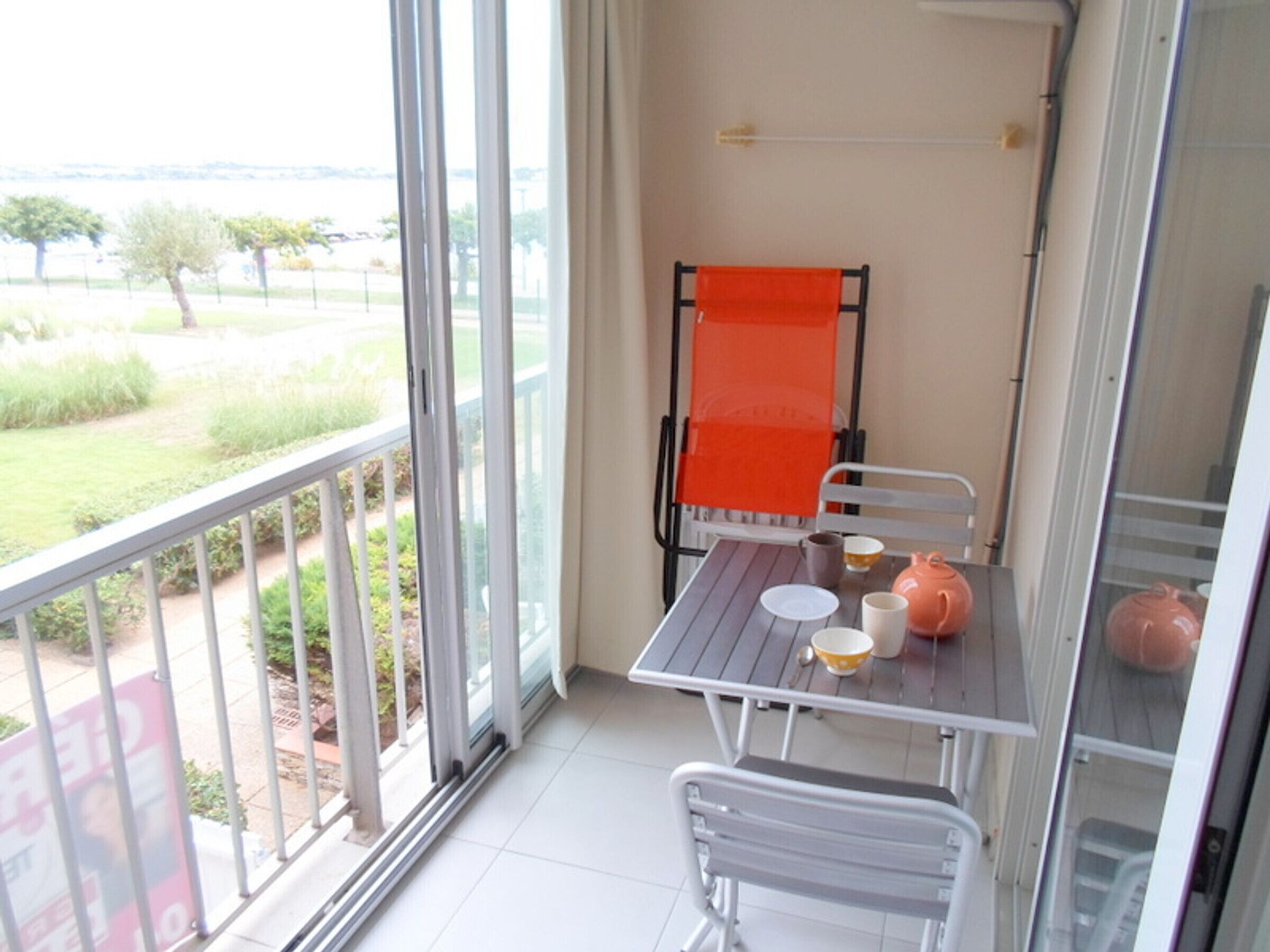 Ein Balkon mit Tisch und Stühlen, Blick auf Grünflächen und ein Gebäude gegenüber dem Wasser.