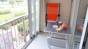 A balcony with a table and chairs, a view of greenery and a building across the water. - Cozy apartment near thermal baths, pets allowed (Balaruc-les-Bains)