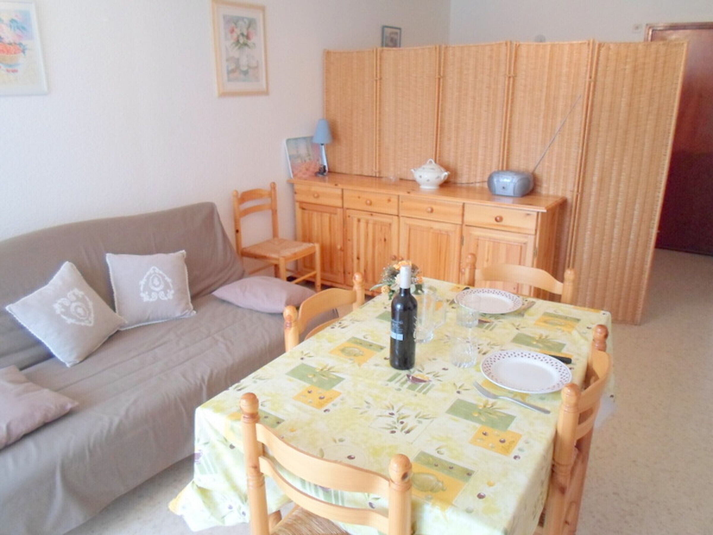 A dining area with a table set for two, a wooden cabinet, and a sofa with cushions.