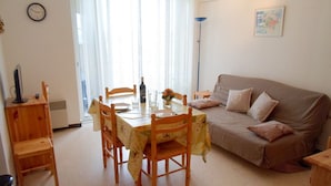 A living room with a dining table, chairs, a sofa, and a clock on the wall. - Cozy apartment near thermal baths, pets allowed (Balaruc-les-Bains)