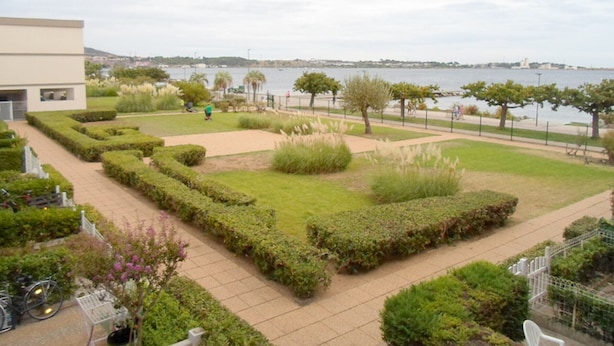 A landscaped garden with pathways, a body of water, and a distant view of a cityscape. - Cozy apartment near thermal baths, pets allowed (Balaruc-les-Bains)