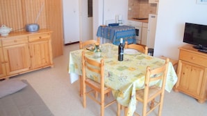 A compact kitchen with wooden cabinets, a dining table with chairs, a television, and a small refrigerator. - Cozy apartment near thermal baths, pets allowed (Balaruc-les-Bains)