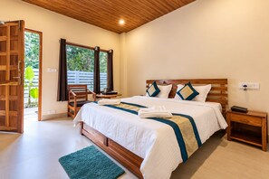 A bedroom with a wooden bed, a nightstand, a chair, and a view of greenery through the window. - Hotel Golden Pebble (Port Blair)
