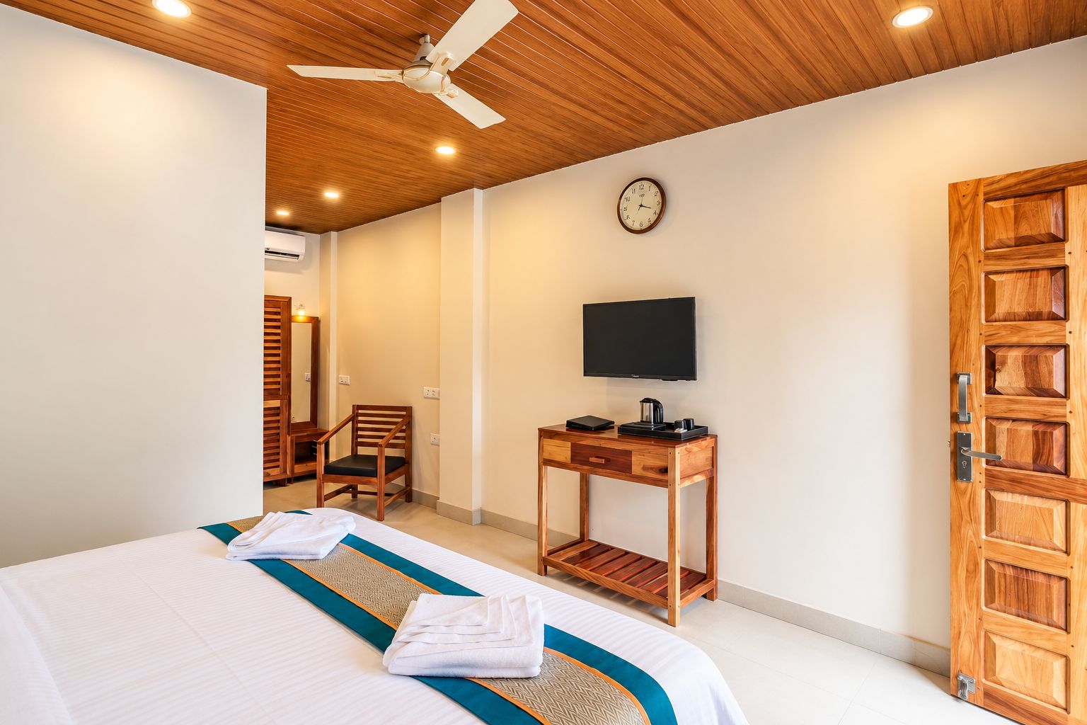 A hotel room with a bed, a desk with a television, a chair, and a wooden door.