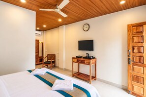 A hotel room with a bed, a desk with a television, a chair, and a wooden door. - Hotel Golden Pebble (Port Blair)