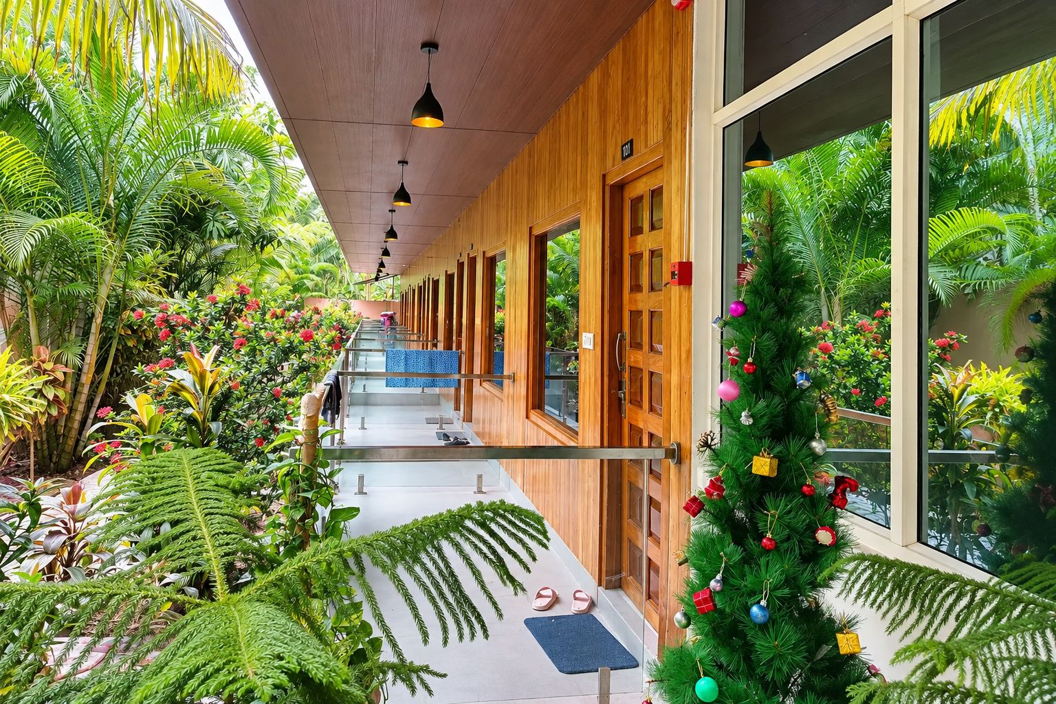Un couloir aux murs en bois, aux portes en verre et où se trouve un sapin de Noël décoré.