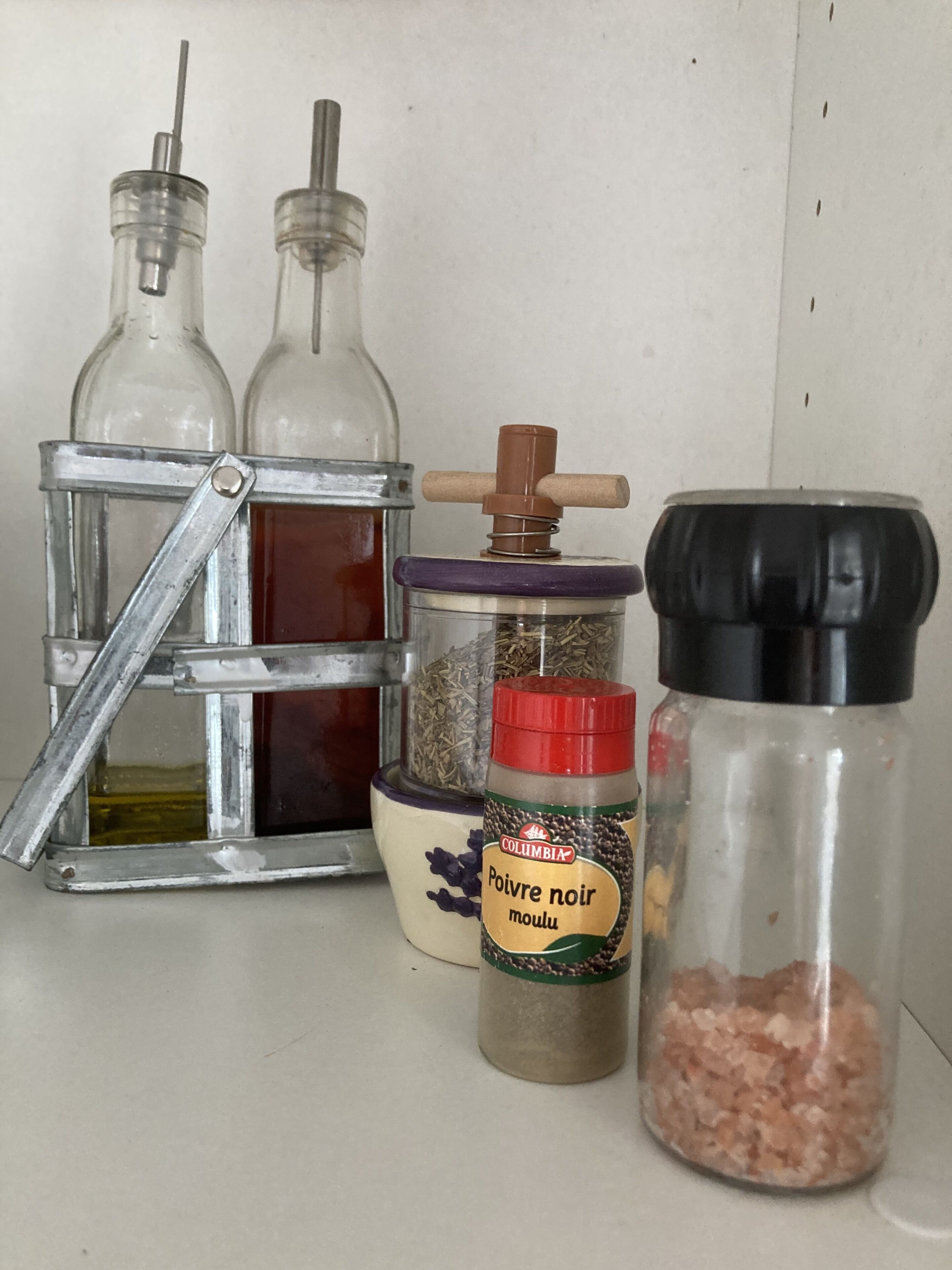 A collection of glass containers with lids, including a metal rack holding two bottles, a jar with a red label, and a black-lidded jar.