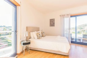 A bedroom with a bed, bedside table, lamp, and a view through a large window.