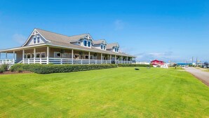 A large, two-story building with a covered porch and a well-maintained lawn. - Show Boat - Kitty Hawk MP 2.5, Pool, Hot Tub, Rec Room, Pool Table, Golf Course Views (Kitty Hawk)