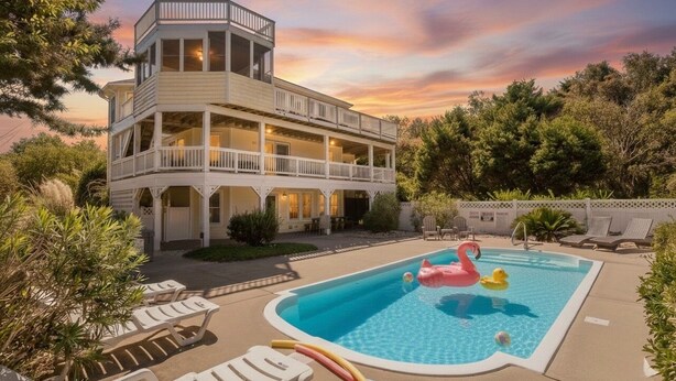 A two-story house with a pool, lounge chairs, and a sunset view. - Show Boat - Kitty Hawk MP 2.5, Pool, Hot Tub, Rec Room, Pool Table, Golf Course Views (Kitty Hawk)