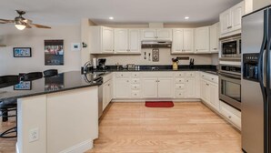 A modern kitchen with white cabinetry, a black countertop, stainless steel appliances, and a wooden floor.