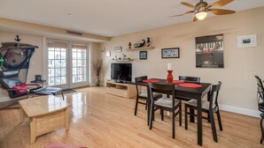 A spacious living room with a wooden floor, a dining table with chairs, a TV, and a ceiling fan.
