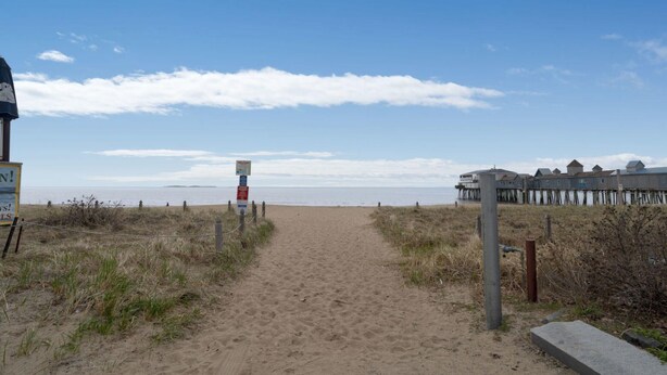 A sandy beach path leading to a pier with a signpost.