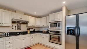 A modern kitchen with white cabinetry, a stainless steel refrigerator, a built-in oven, and a microwave.