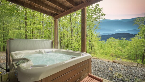Un bain Ă remous dotĂ© de bancs en bois, installĂ© dans un cadre idyllique avec une forĂȘt et des montagnes en arriĂšre-plan.