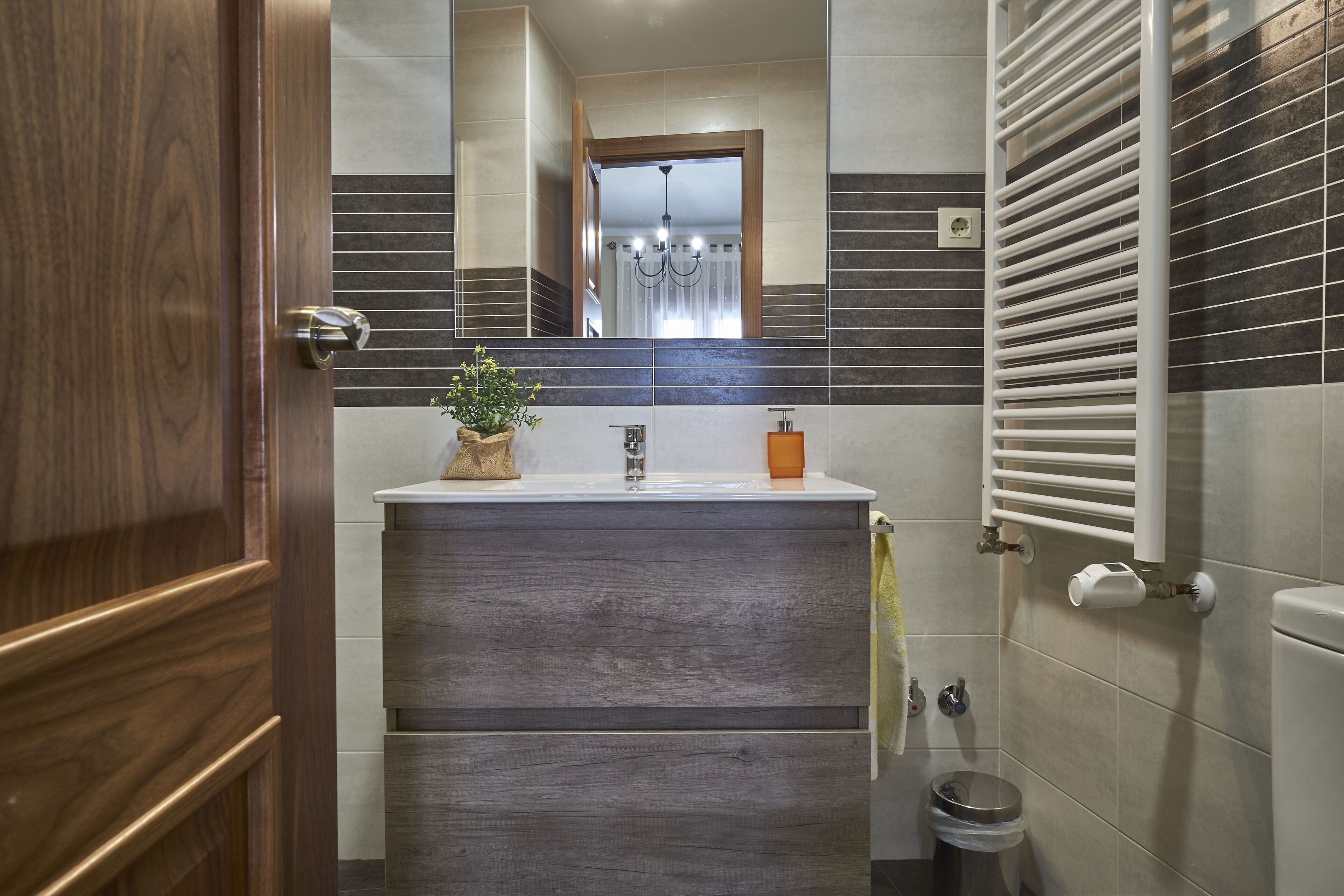 A bathroom with a wooden door, a sink with a plant, a towel, a toilet, and a towel rack.