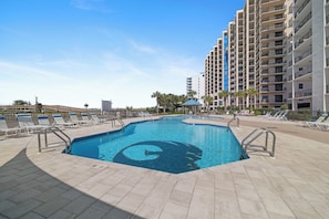 Piscina com espreguiçadeiras, um gazebo e um edifício alto ao fundo.