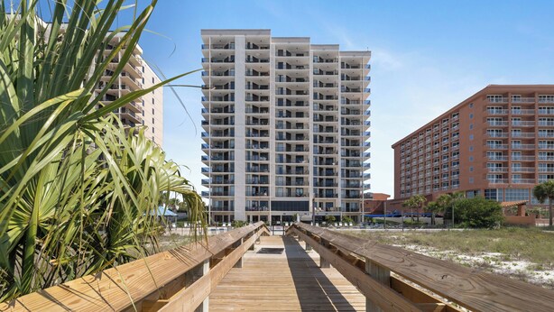 Un hotel de varios pisos con balcones, un paseo marítimo de madera y cielo despejado.