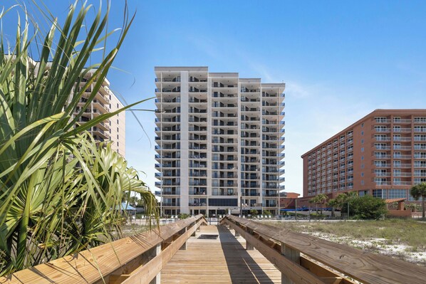 A multi-story hotel with balconies, a wooden boardwalk, and a clear sky.