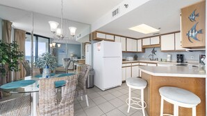 Una cocina moderna con una isla central, un comedor con sillas de mimbre y vista al océano.