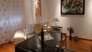 Ein modernes Wohnzimmer mit einem Glastisch, gemusterten Kissen, einem Beistelltisch mit Lampe und abstrakter Kunst an den Wänden.