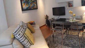 Ein modernes Wohnzimmer mit einer Couch, einem Esstisch mit Stühlen, einem Flachbildfernseher und einem Bücherregal.