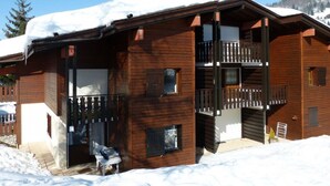 A wooden chalet with a balcony, a garage door, and a snow-covered roof. - Quiet 3-Room Duplex with Covered Parking, Balcony, Near Ski Slopes (La Clusaz)