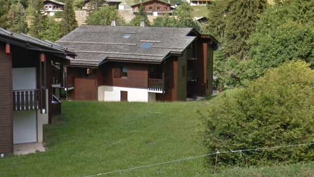 A hillside residential area with multiple wooden houses, some with balconies and large windows, surrounded by greenery. - Quiet 3-Room Duplex with Covered Parking, Balcony, Near Ski Slopes (La Clusaz)