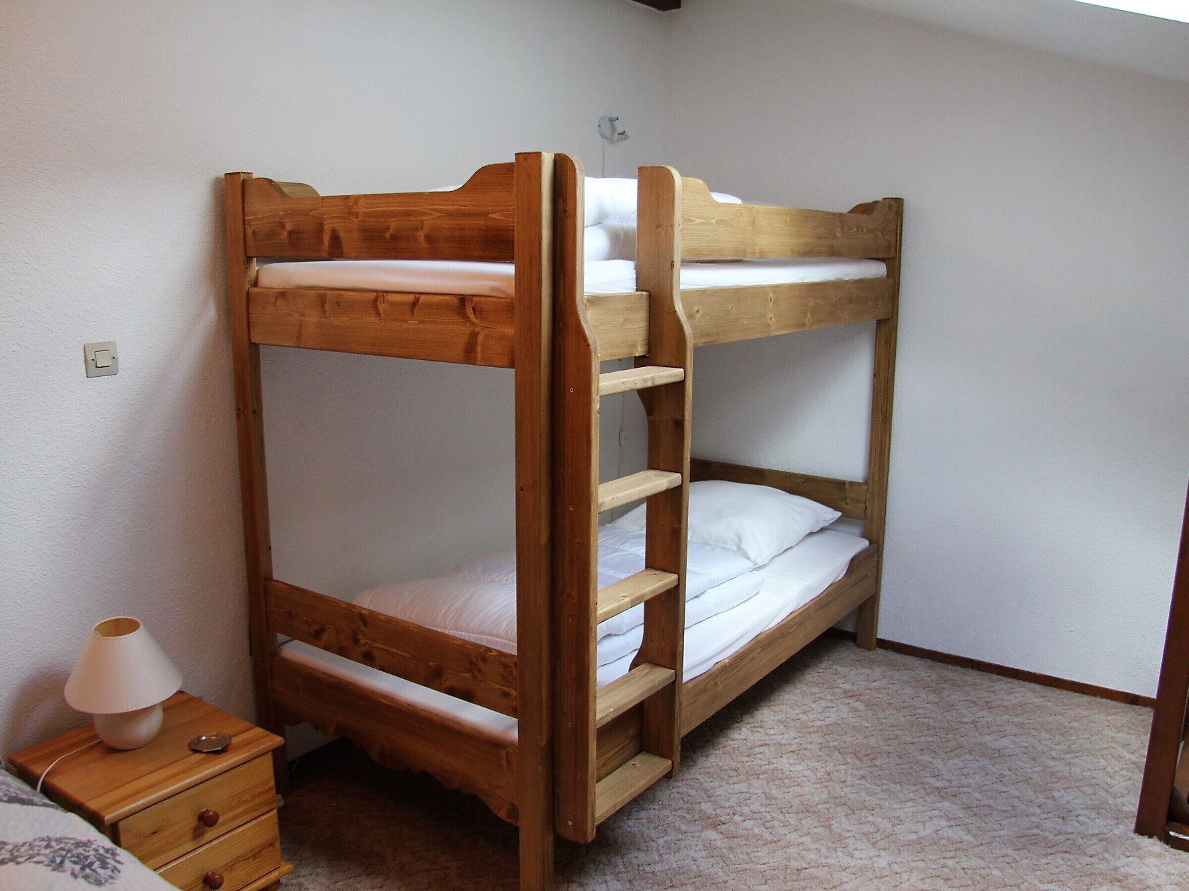 Ein Etagenbett mit Holzrahmen, ein Nachttisch mit Lampe und ein Teppichboden.