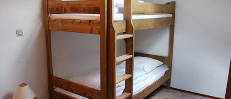 A bunk bed with a wooden frame, a bedside table with a lamp, and a carpeted floor.