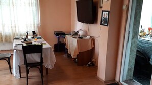 Un coin repas avec une table dressée pour deux personnes, un téléviseur fixé au mur et une cheminée visible à travers une porte ouverte.