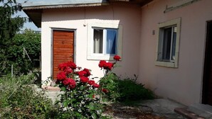 Un bâtiment d’un seul étage, doté d’une porte et de fenêtres en bois, entouré de verdure et de fleurs rouges.
