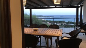 Un patio al aire libre con una mesa de madera y sillas de mimbre, con vistas a la costa.