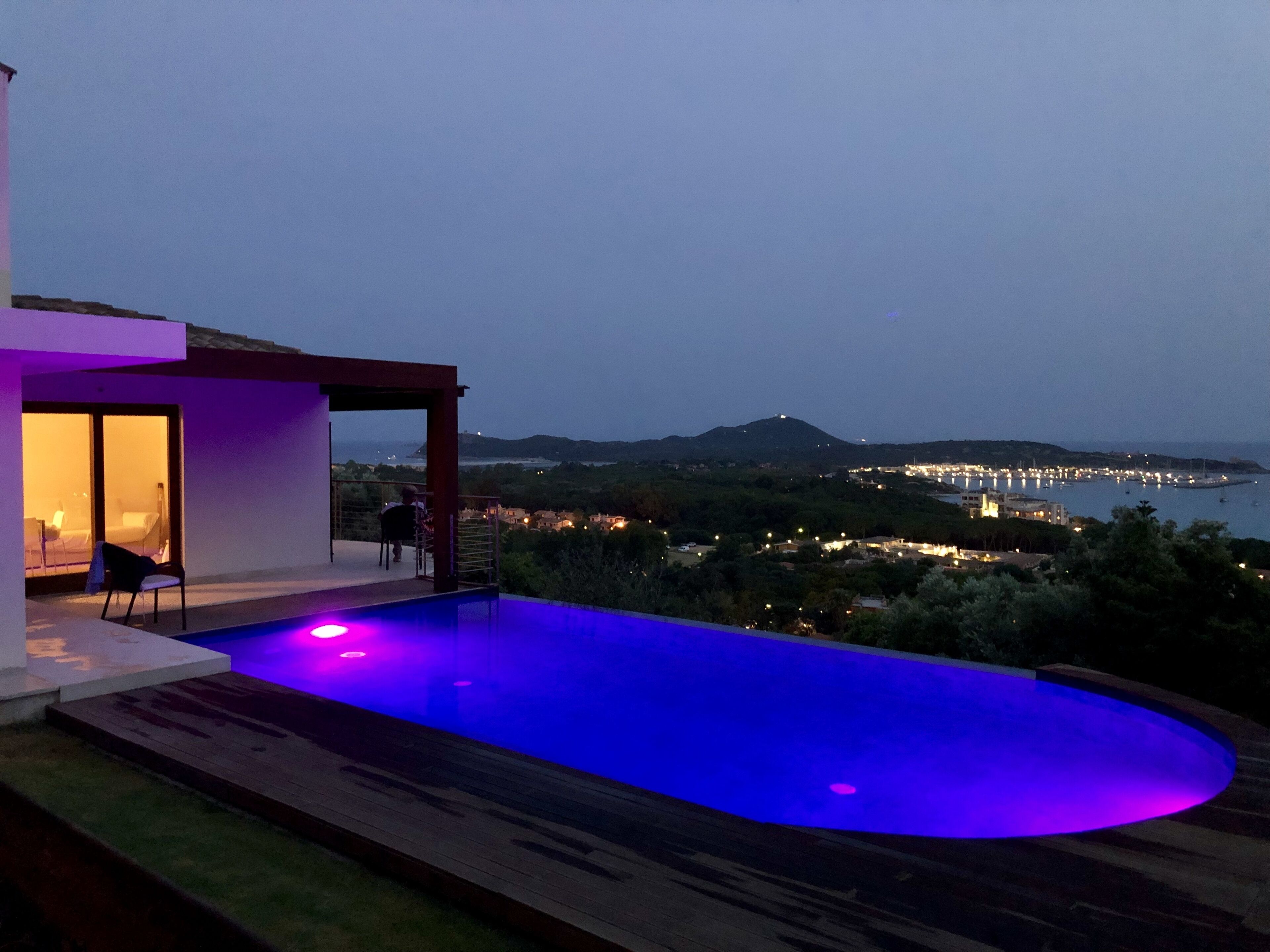 Un espace piscine extérieur moderne, offrant une vue sur une ville côtière au crépuscule.