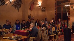 A group of people seated at a table in a warmly lit room with patterned walls and a large window. - Guest House The Dor fibula (Aït Ben Haddou)