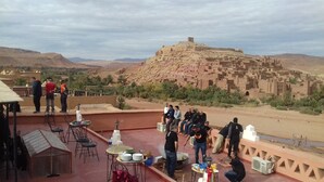 A terrace with tables and chairs, overlooking a traditional village and mountains. - Guest House The Dor fibula (Aït Ben Haddou)