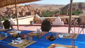 A dining table set outdoors with a view of a traditional village in the background. - Guest House The Dor fibula (Aït Ben Haddou)