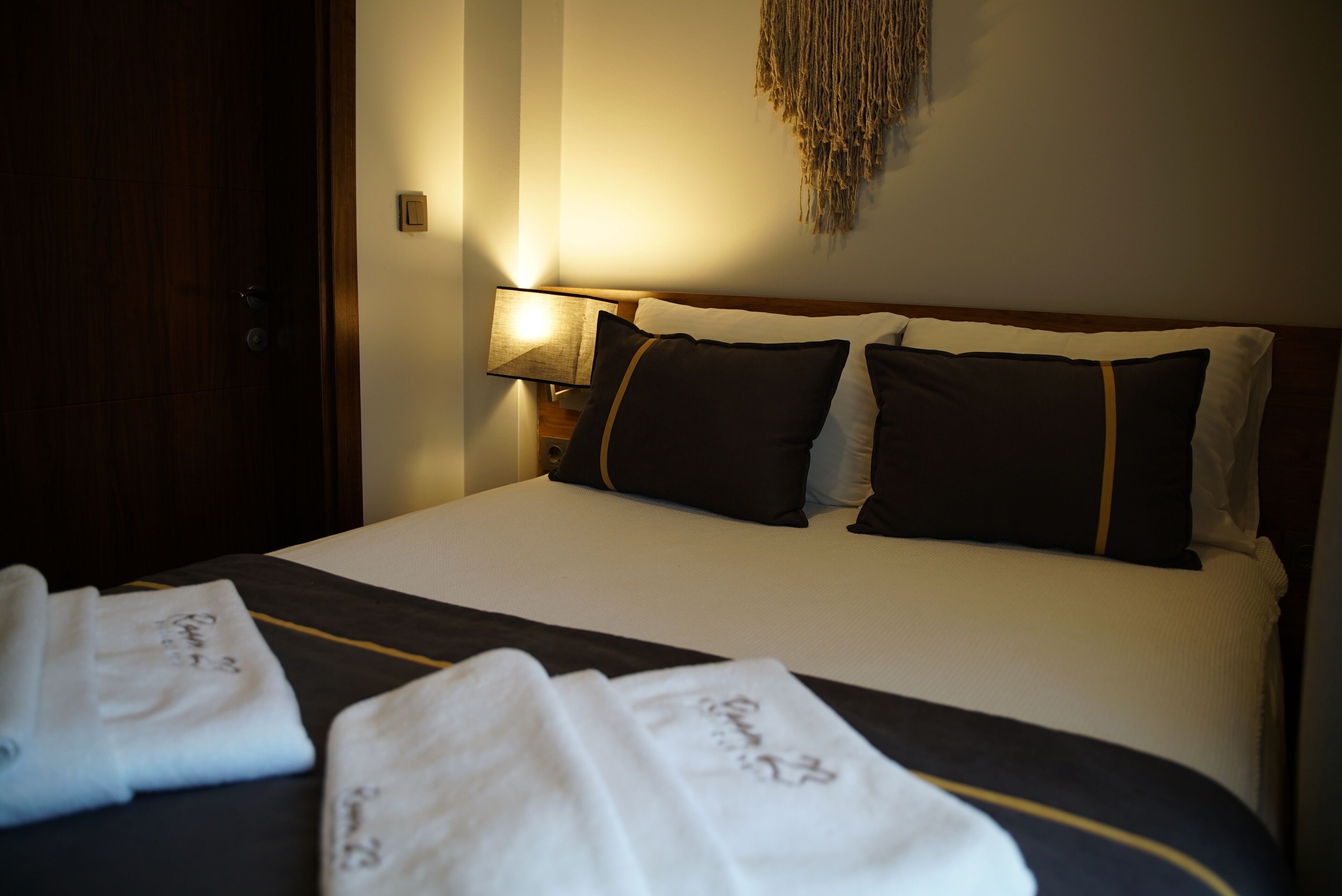 A neatly made bed with white and dark bedding, a bedside lamp, and a wall-mounted decorative piece.