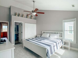 A bedroom with a bed, a ceiling fan, a wardrobe, a desk, and a window.