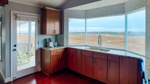 A kitchen with wooden cabinets, a window with a view of a flat landscape, and a door leading to an outdoor area.