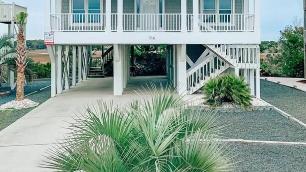 A two-story beachfront house with a balcony on each floor, a covered entryway, and a number '716' on the front.