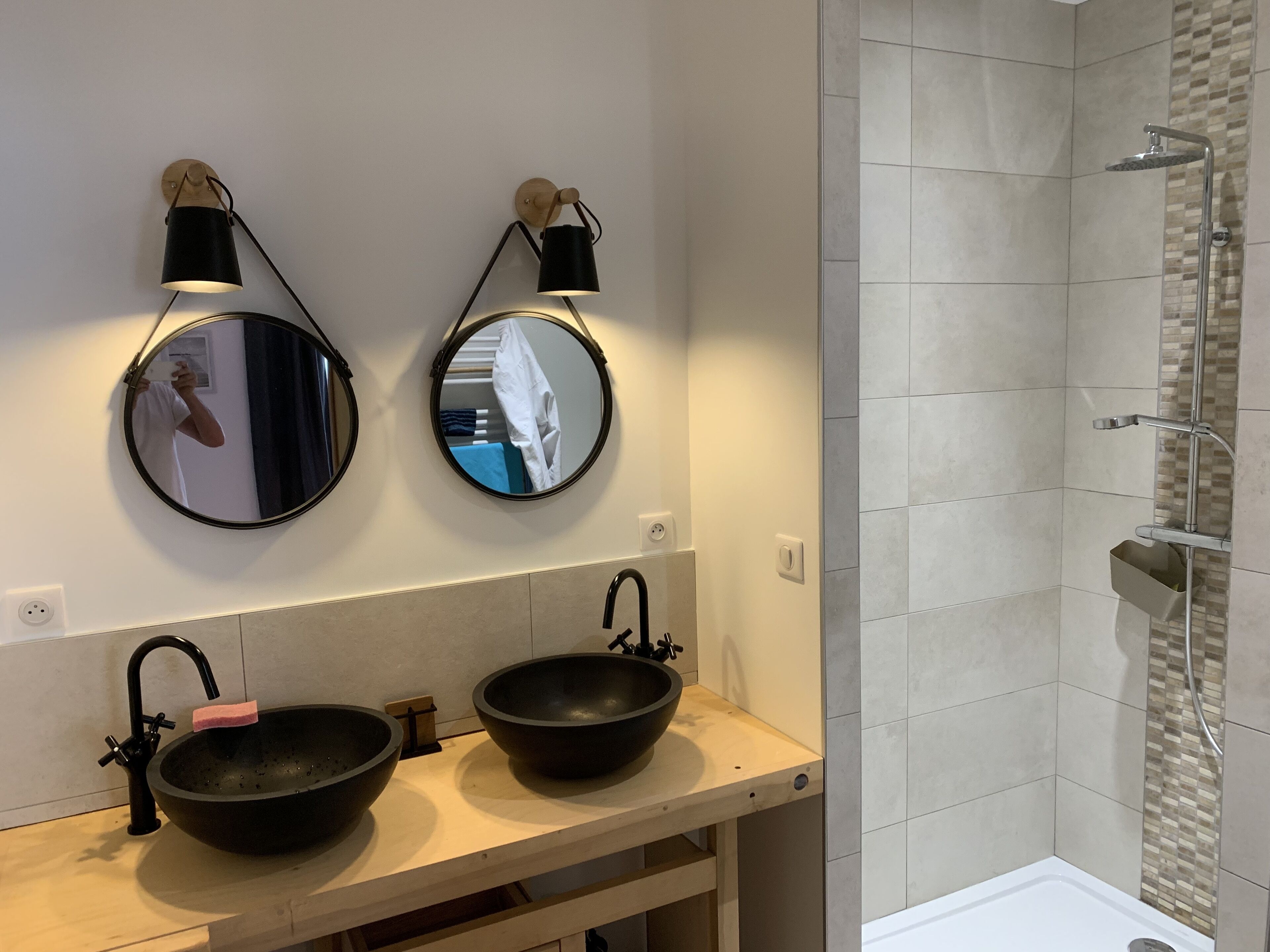 Une salle de bain avec deux miroirs ronds, un lavabo noir et un espace douche.
