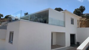 A modern two-story house with a glass balcony, a small window, and a door leading to an outdoor area.