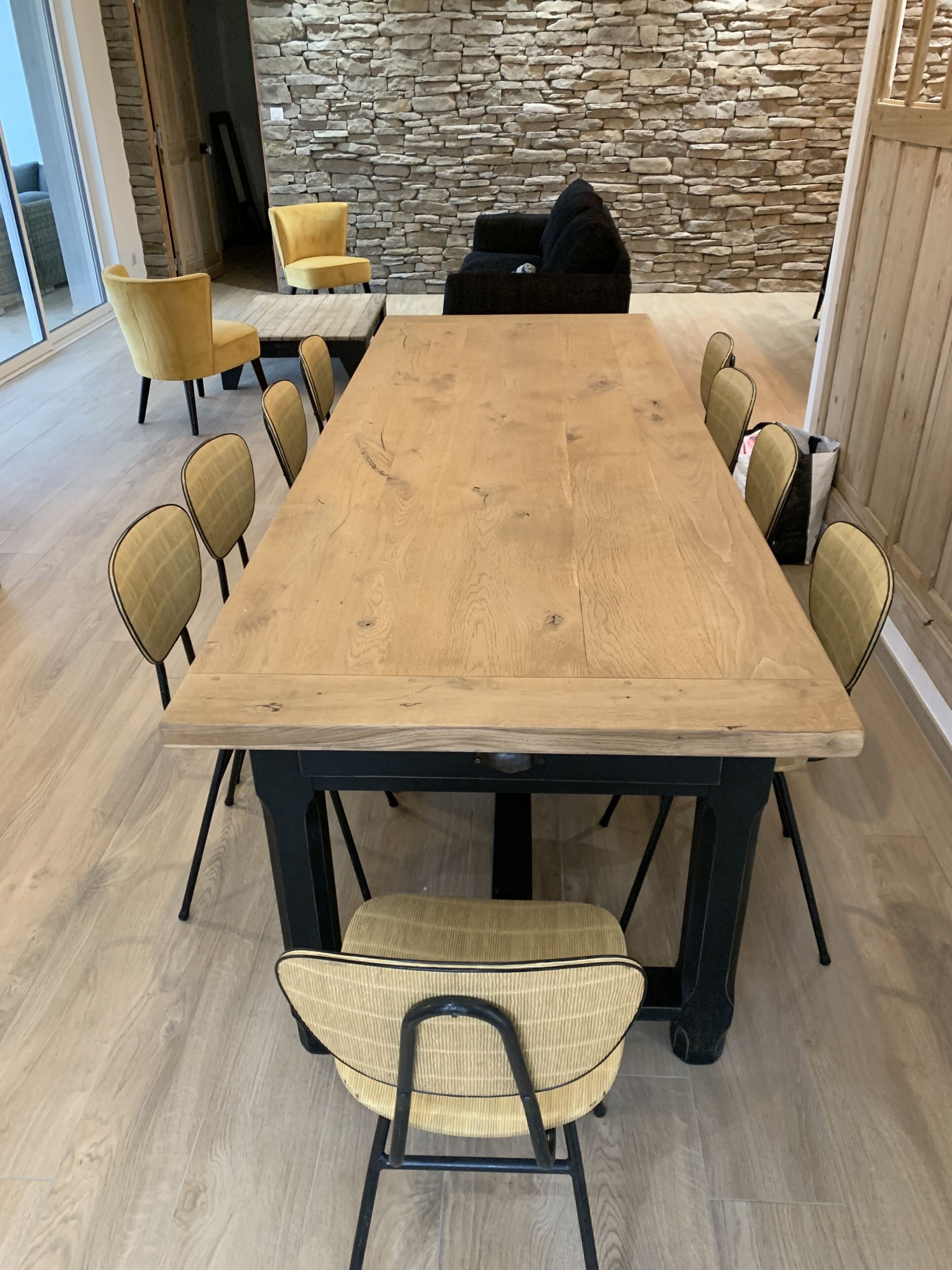 Una gran mesa de madera para comer con ocho sillas, una pared de piedra y una puerta de madera en una habitación con piso de madera clara.