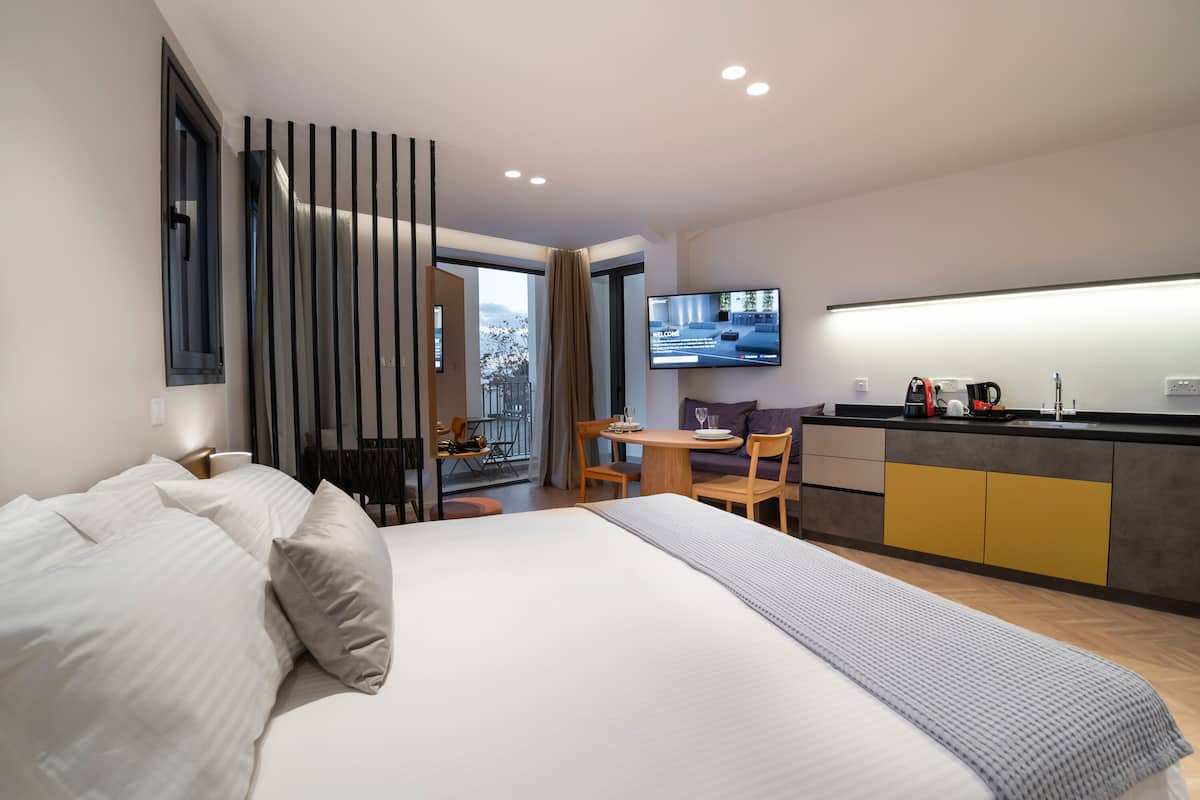 A modern hotel room with a large bed, a dining area, and a TV displaying a welcome message.