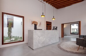 A modern reception desk with a large window, a potted plant, and artwork on the wall. - Alinea Suites Limassol Center (Limassol)